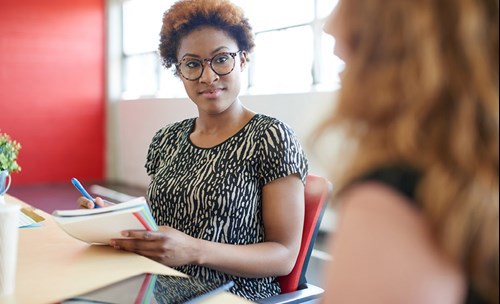 Two woman talking, one person taking notes