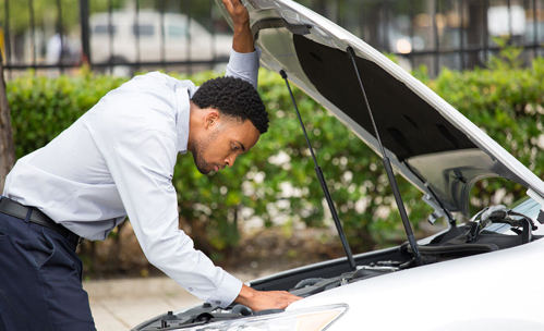 Man looking at the mechanics off a car, under the hood of the car