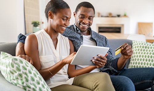 Woman and man sitting on couch, using tablet while holding a bank card
