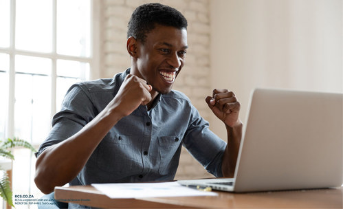 Smiling man fist-bumping in the air, looking at a laptop