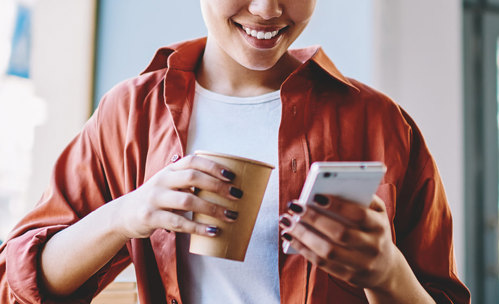 Woman with coffee cup in her hand, smiling at her phone in her other hand