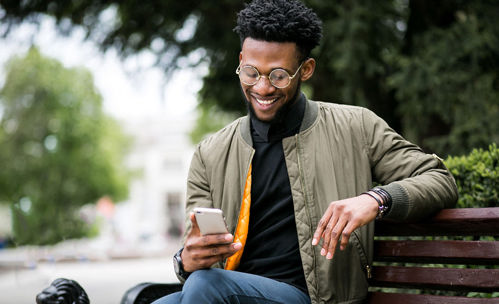 Smiling man sitting on a park bench, while looking at his phone