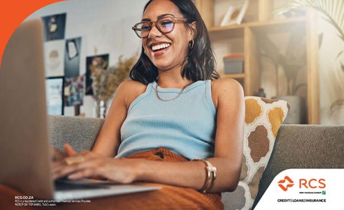 Smiling woman sitting on a couch, working on laptop.