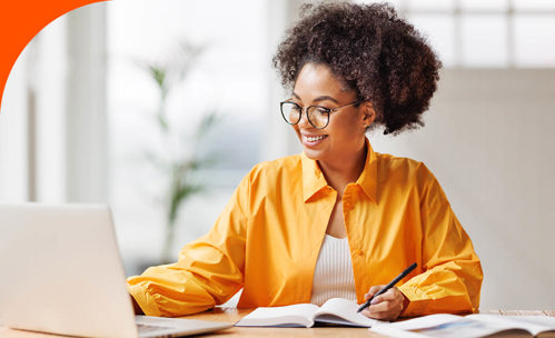 Smiling woman working on a laptop with books in front of her.