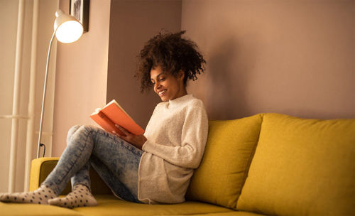 Woman reading a book on a couch next to lamp