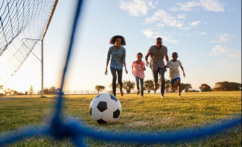 Family playing soccer, running to ball that's in the net