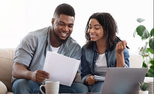 Man and woman sitting on couch, looking at documents, smiling