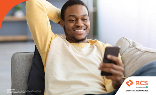 Smiling man sitting on a couch, busy on his phone.